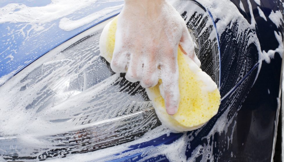 Man Washing A Soapy Blue Car with a Yellow Sponge